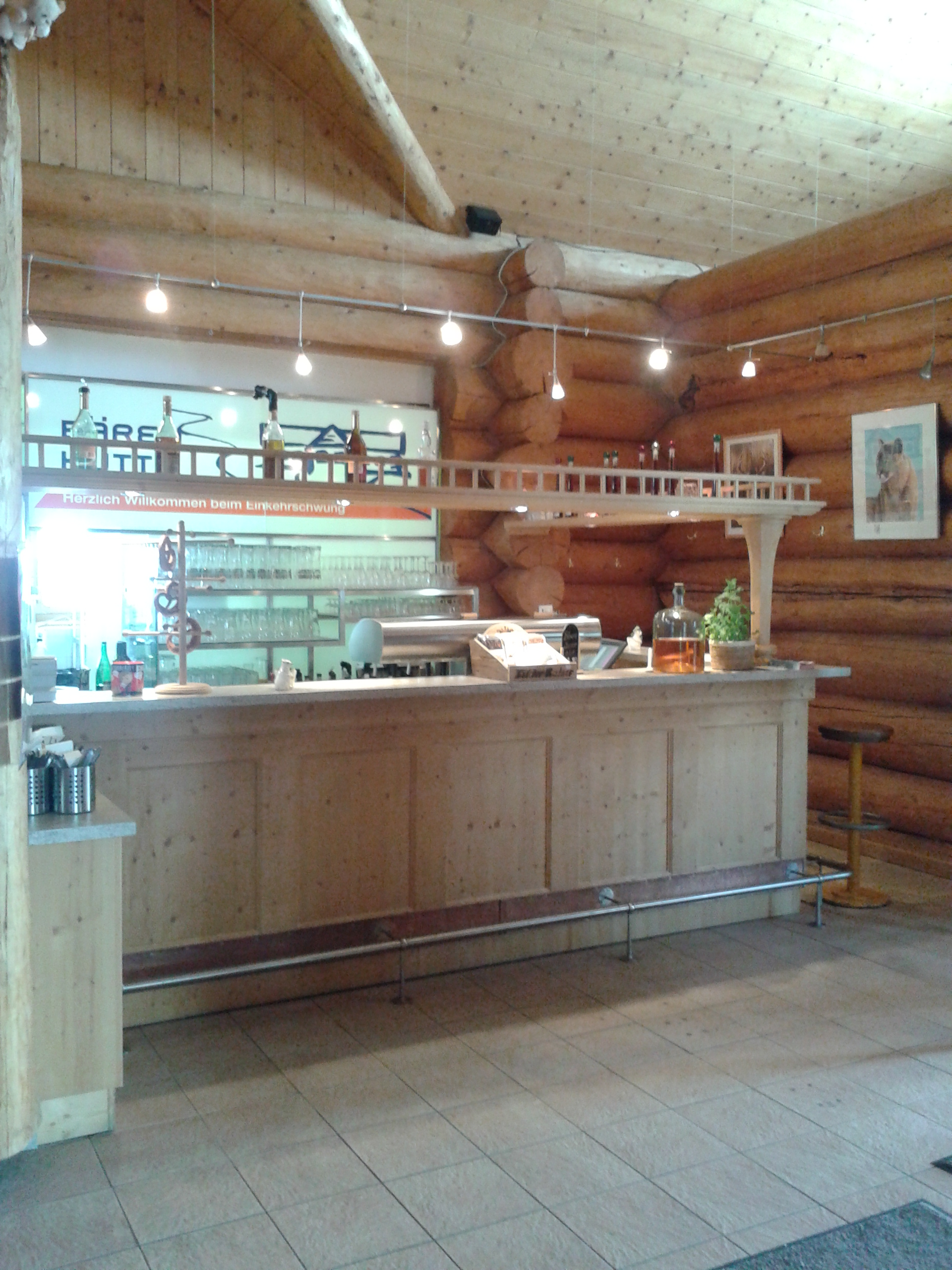 Eine Bar mit Tresen in hellem Holz mit Blick in die Küche.